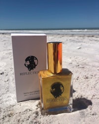 a bottle of gold perfume on a beach next to the ocean